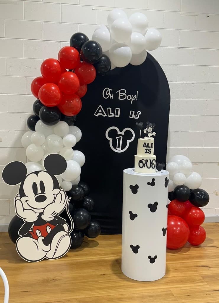 Mickey Mouse first birthday with black arch backdrop, balloon garland, and themed cake